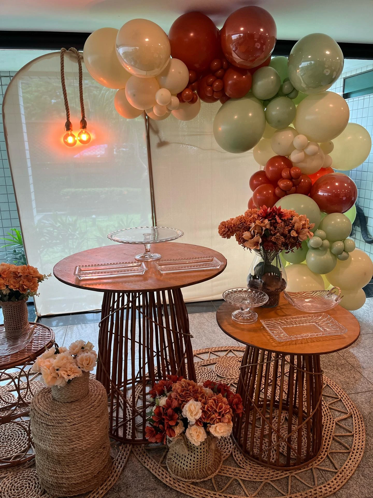 Composição boho com balões terracota, verde e areia, mesas de vime e arranjos secos.