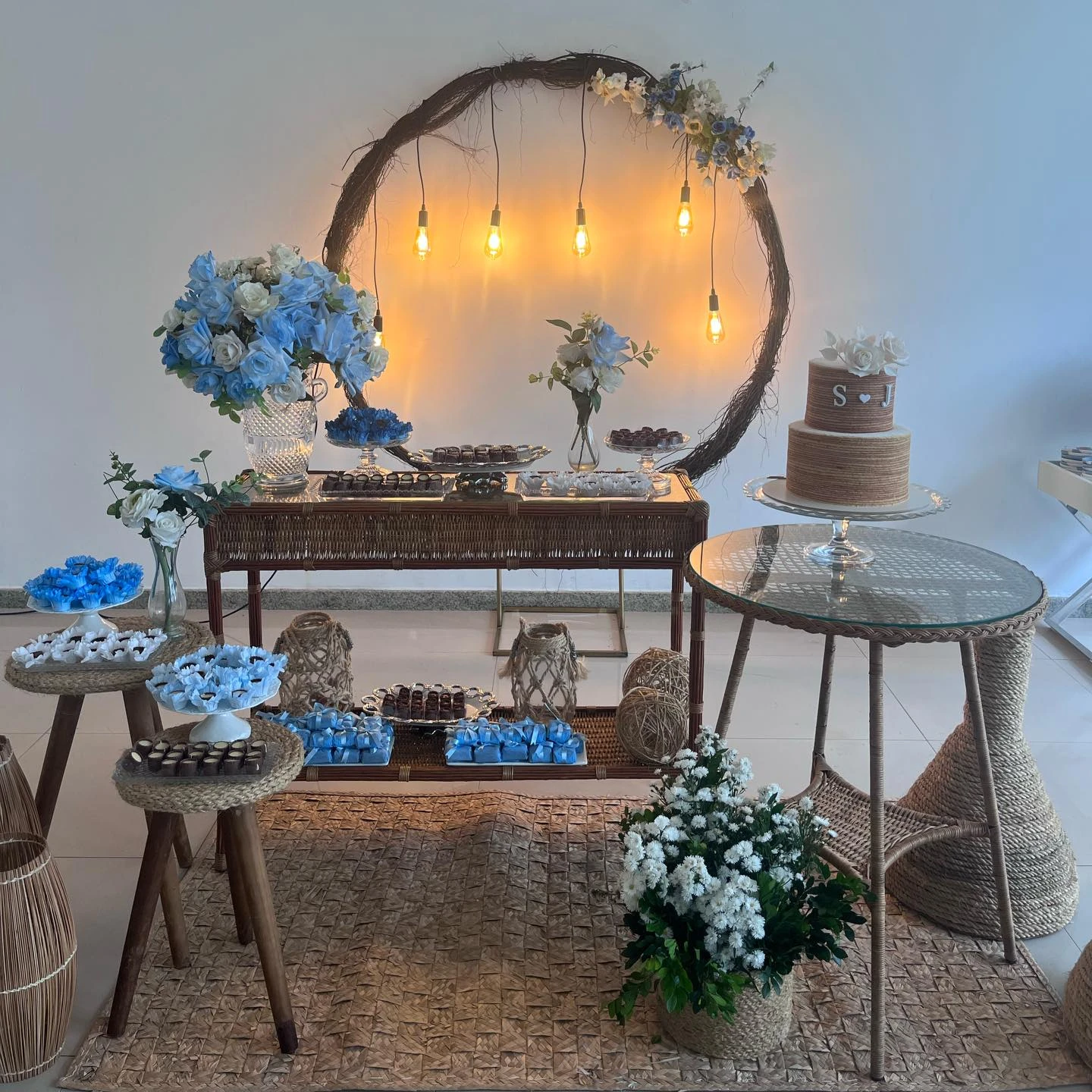 Mesa de casamento com flores azuis, móveis de madeira, painel circular e lâmpadas pendentes.